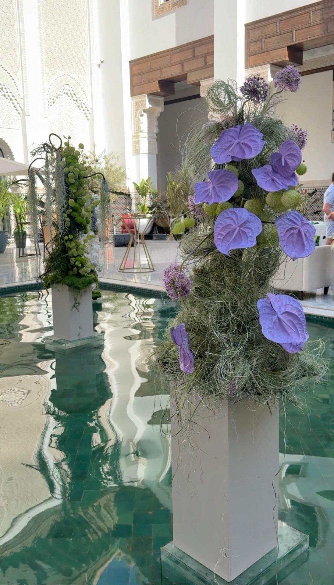 Gala Dinner Vegetal Garden at the patio of the Oberoi Marrakech — purple vanda orchids and anthuriums on white plinths above the emerald reflecting pool, ivory lounges and brass lanterns, produced by SBAI Events Production