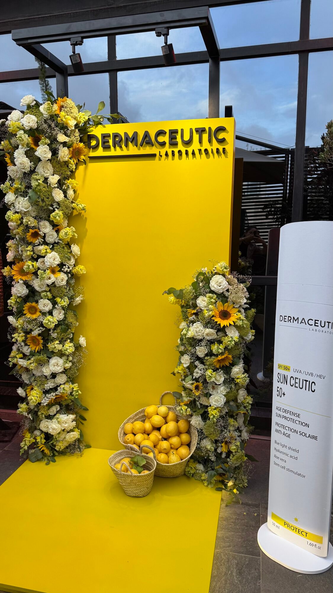 Dermaceutic product launch in Casablanca — yellow branded photo wall framed by white roses, sunflowers and lemon baskets, produced by SBAI Events Production