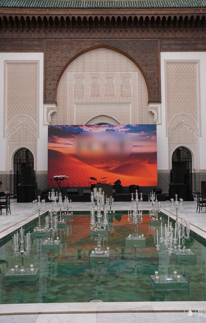 Crystal candelabras on mirrored plinths standing in a green-tiled reflecting pool beneath a monumental Moroccan arch, staged by SBAI Events Production