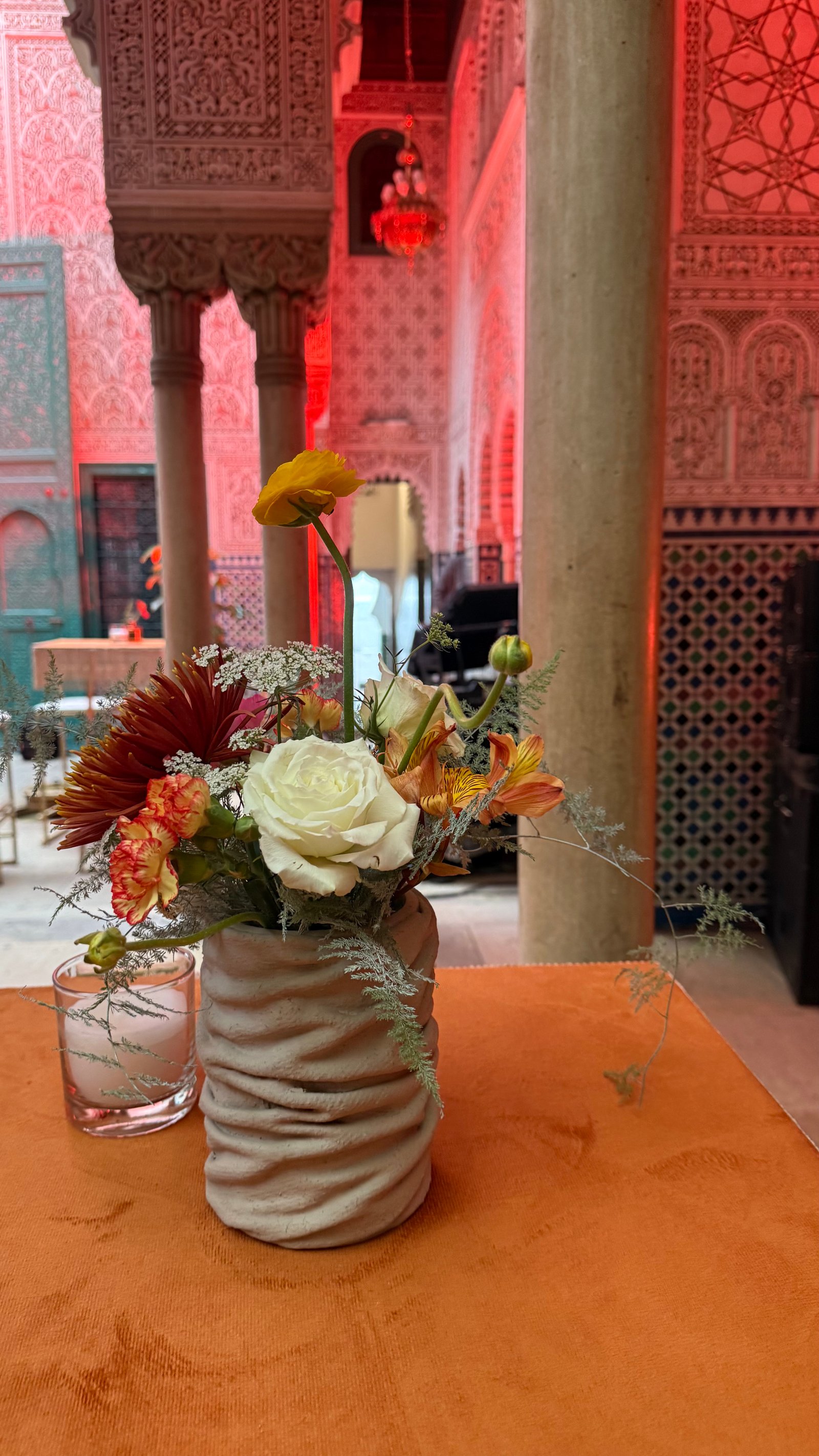 Corporate event for Orange at the Mahkama du Pacha in Habous, Casablanca — orange linens, terracotta vases with ranunculus and gerbera, candlelight and carved Moorish arches, produced by SBAI Events Production