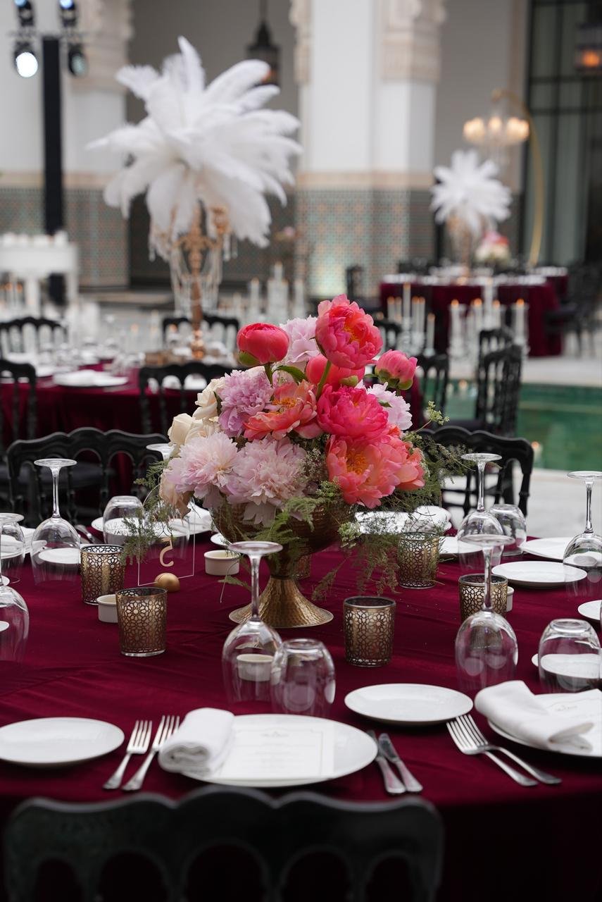Burgundy velvet round table with coral peony centerpiece and white ostrich feather displays overlooking a green reflecting pool, styled by SBAI Events Production